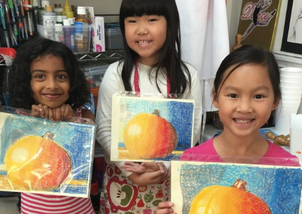 Three kids smiling at the camera and showing three paintings